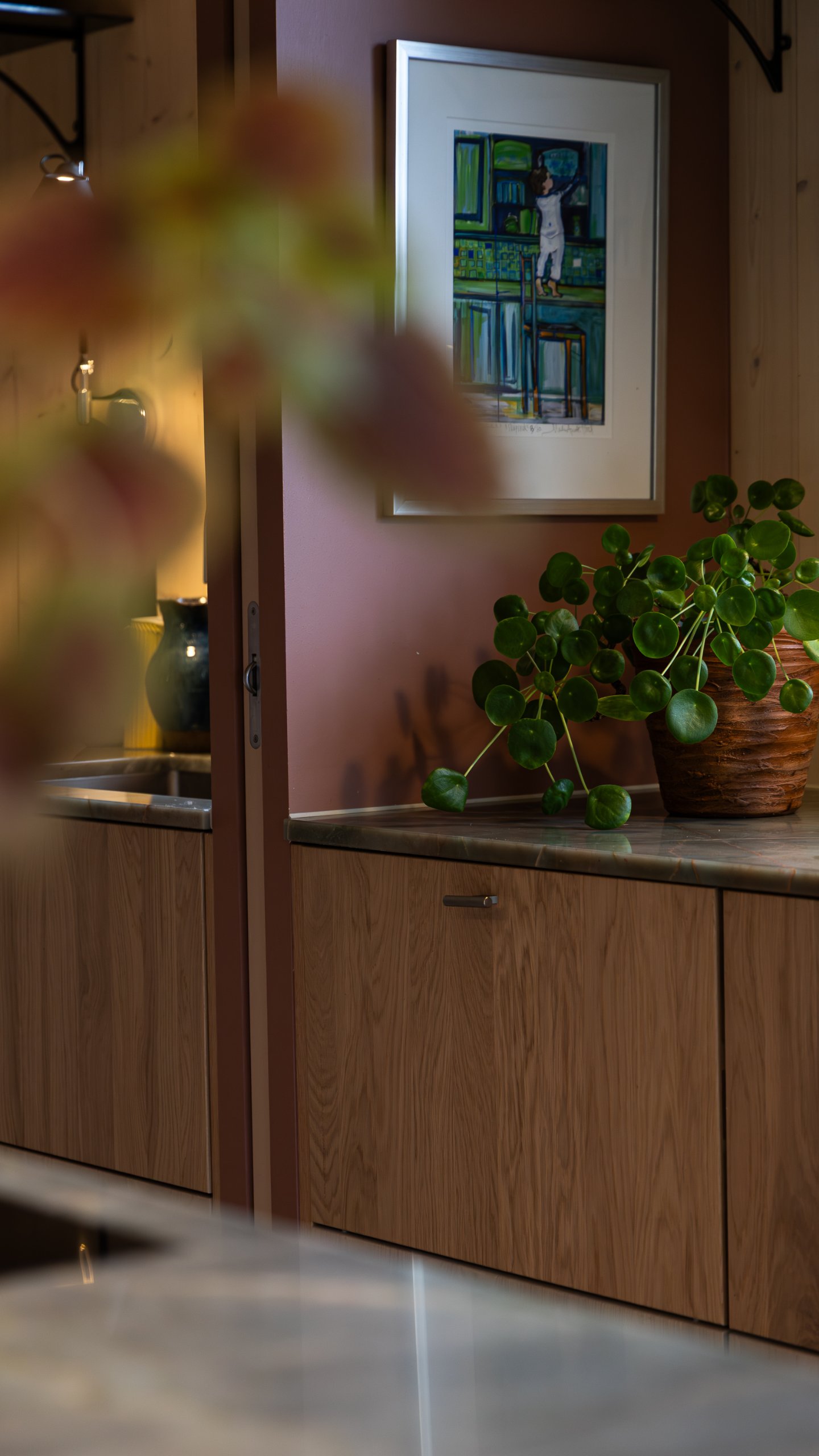 Trefronter og steinbenker på begge sider av skyvedørens karm, med et bilde og en potteplante ved siden av. Trefronter og steinbenker på begge sider av skyvedørens karm, med et bilde og en potteplante ved siden av.